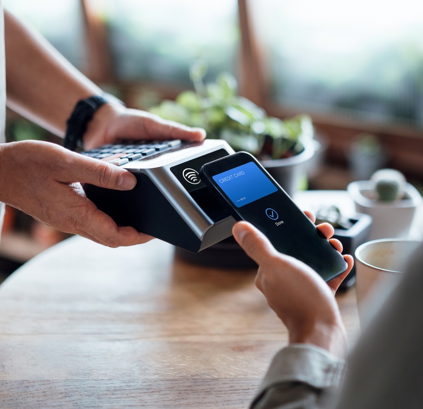 Customer using contactless mobile payment at a point-of-sale terminal supported by secure financial IT solutions