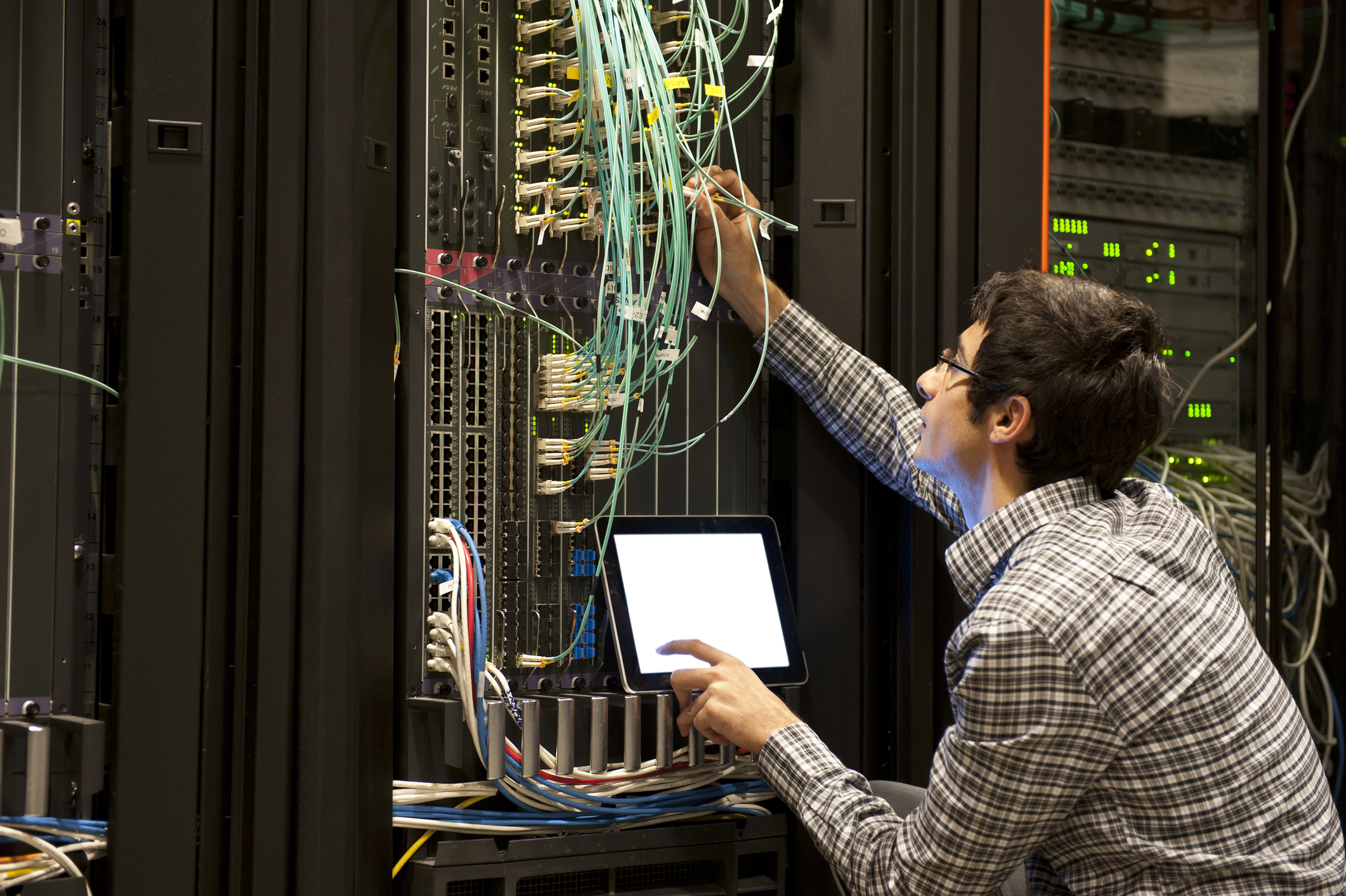 IT engineer checking network cabling in a data center while working through a recovery checklist on a tablet